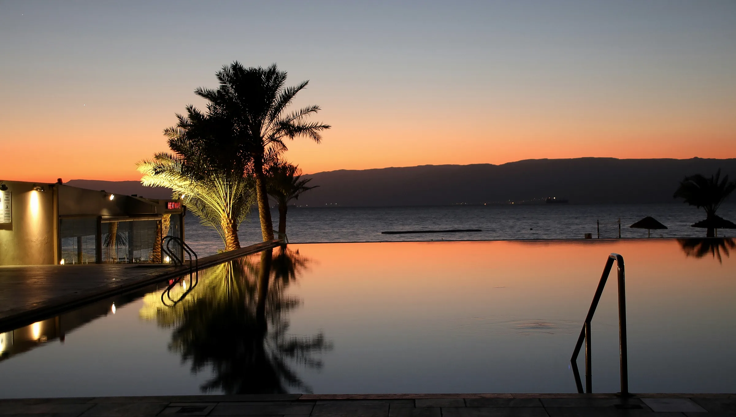 Infinity pool at dusk overlooking the sea, palms in silhouette