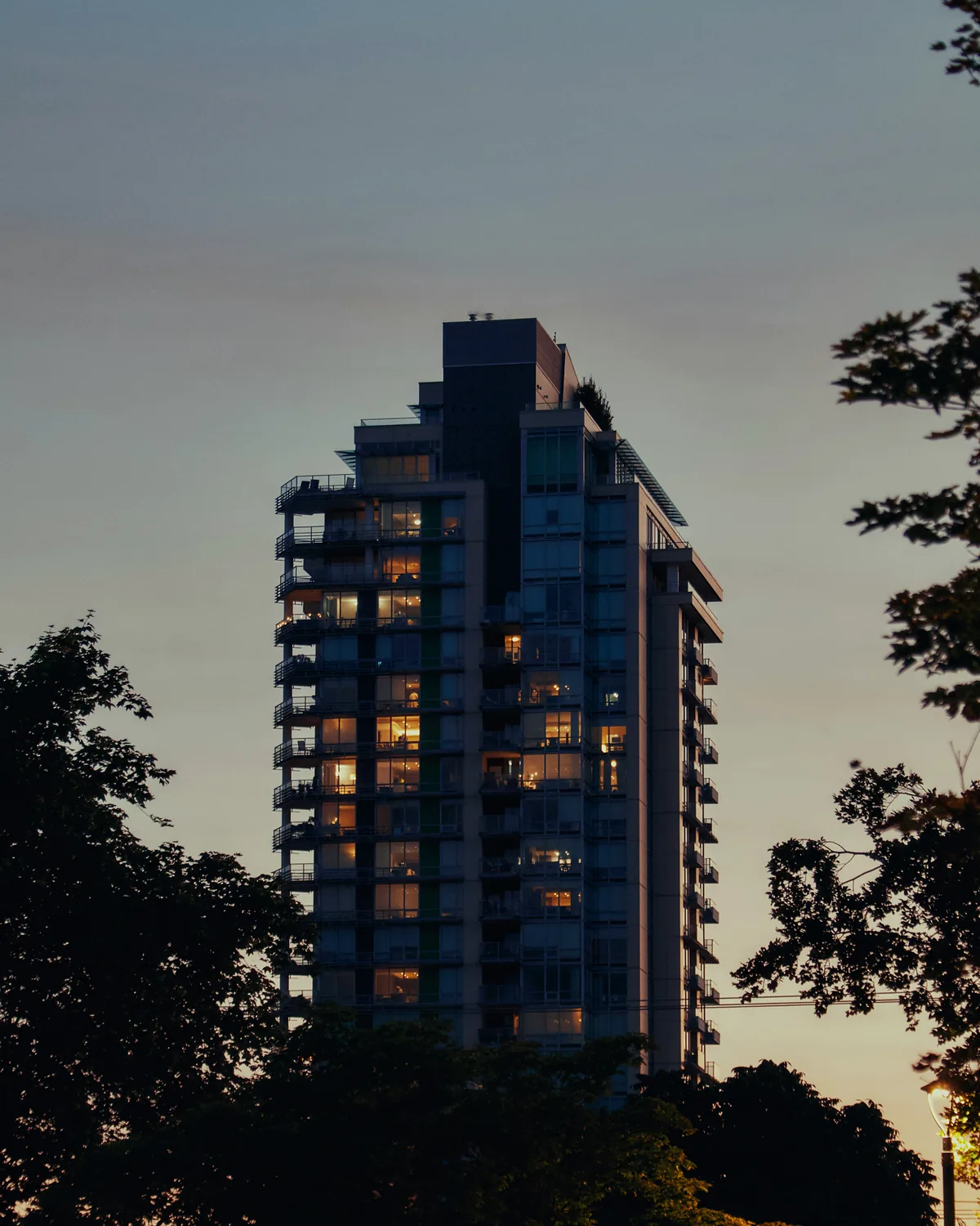 Residential tower at dusk with lit windows, framed by trees