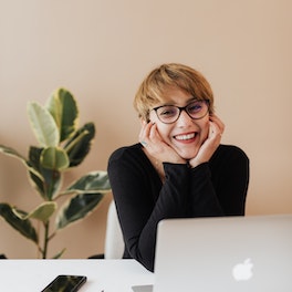 Cheerful woman smiling while sitting at table with laptop