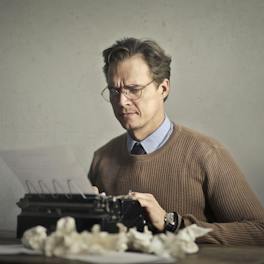 Adult frowned male writer working on typewriter at home